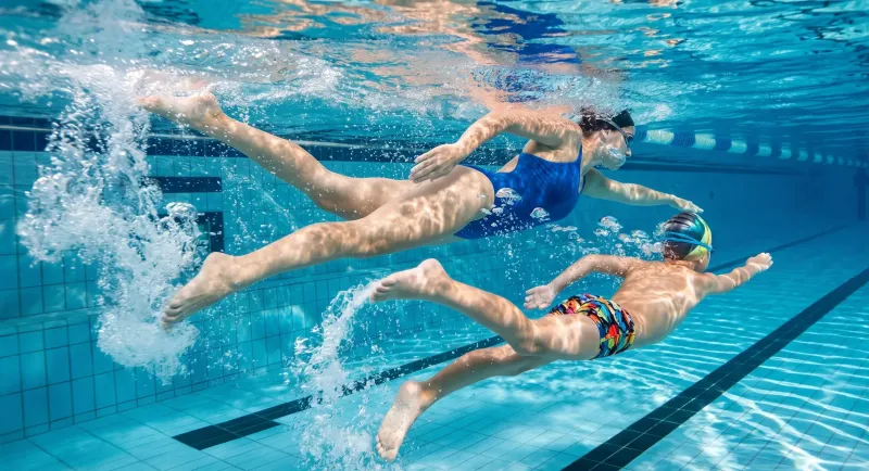 Schwimmtrainerin und Kind tauchen gemeinsam unter Wasser durch das Becken